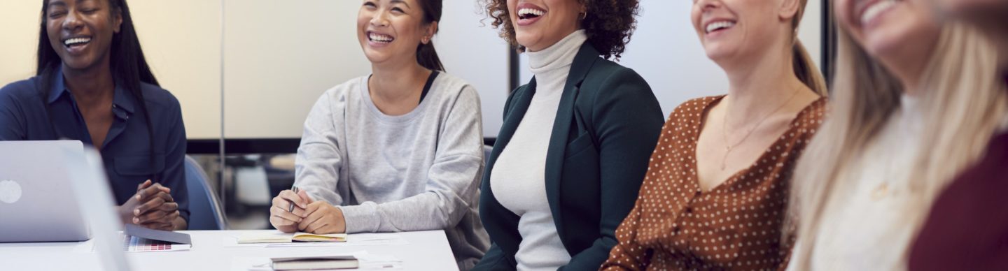 Line Of Businesswomen In Modern Office Listening To Presentation By Colleague