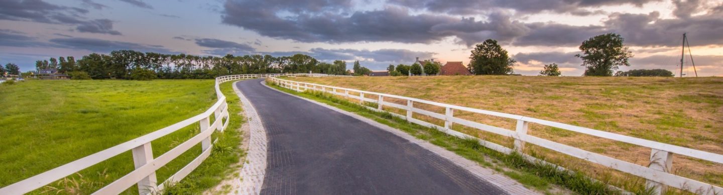 Curved road with white fences leading to village